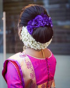 a woman wearing a pink and yellow sari with flowers in her hair is seen from the back