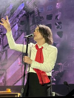 a man in white shirt and red tie holding up his hand while standing next to a microphone