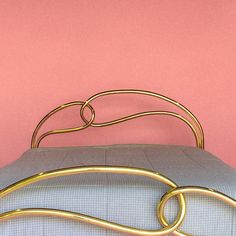 a gold metal bed frame against a pink wall