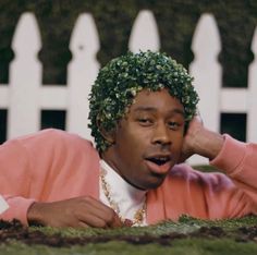 a man laying on the ground in front of a white fence wearing a pink sweater