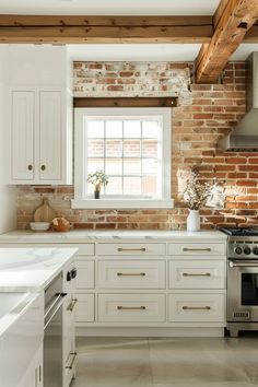 a kitchen with brick walls and white cabinets is pictured in this image, there are two windows above the stove