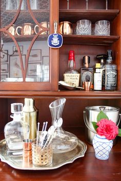 a wooden cabinet filled with bottles and glasses on top of a table next to a vase