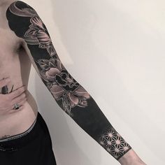 a man with a flower tattoo on his left arm and half sleeve is standing in front of a white wall