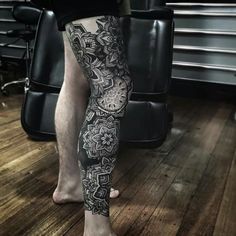 the legs and ankles of a man with tattoos on them, standing in front of a chair