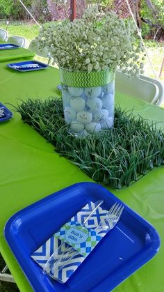 a green table topped with blue plates covered in white flowers and greenery next to a vase filled with baby's breath balls