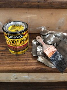 a can of wood finish next to a paint brush on a wooden bench with fabric