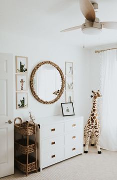 a giraffe standing next to a white dresser in a room with pictures on the wall