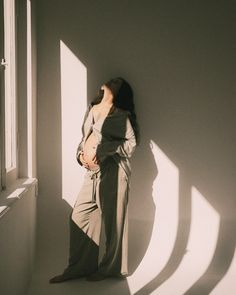 a woman standing in front of a window with her back to the camera and arms behind her head