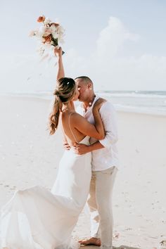 a bride and groom kissing on the beach