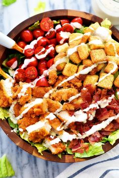 a salad with dressing and tomatoes in a wooden bowl next to a glass of milk