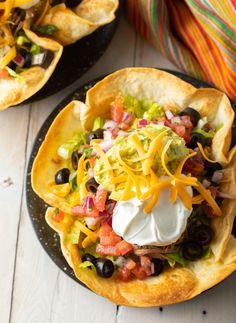 two black plates filled with nachos topped with sour cream and toppings on top