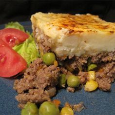 a blue plate topped with meat and veggies next to a slice of cheesecake