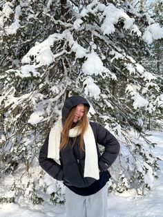 a woman standing in front of a snow covered tree with her hands on her hips