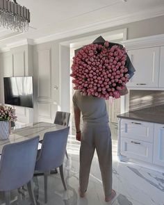 a person with a bunch of flowers on their head standing in front of a dining room table