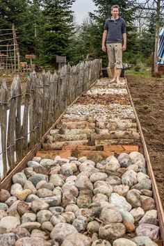 a man standing on top of a pile of rocks next to a wooden fence and trees