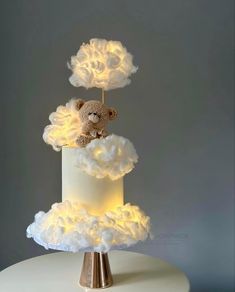 a teddy bear sitting on top of a white cake with clouds and lights in the shape of clouds