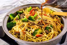 a pan filled with noodles and vegetables being stirred