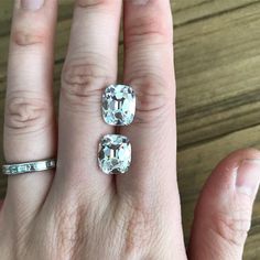 a person's hand with two engagement rings on top of their fingers, and an oval shaped diamond in the middle