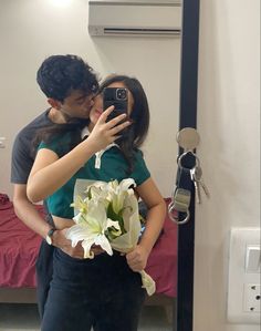 a man and woman taking a selfie in front of a mirror while holding flowers