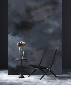 a chair and table with flowers on it in front of a dark wall, against a black background