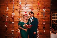 a man and woman standing next to each other in front of a wooden wall with flowers on it