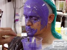 a man with purple paint on his face is painting another person's face in blue