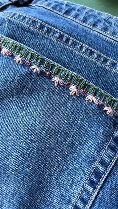 a pair of blue jeans with pink flowers on them and some green trimmings