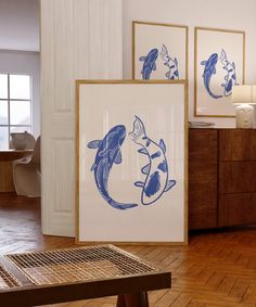 two framed art pieces sitting on top of a hard wood floor next to a wooden table