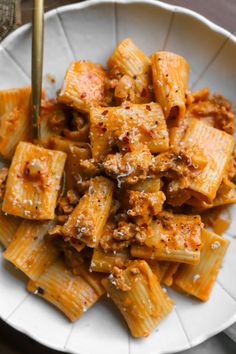 a white plate topped with pasta covered in sauce and seasoning next to a fork