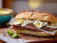 a roast beef sandwich on a cutting board next to a bowl of guacamole