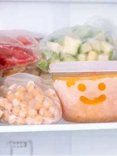 an open refrigerator filled with lots of food and plastic bags on top of the shelves