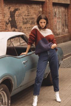 a woman leaning on the hood of an old car in front of a brick building