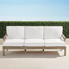 a white couch sitting on top of a cement floor next to a green hedge covered wall