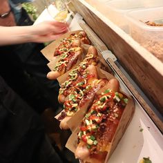 hotdogs with toppings lined up on trays at a food stand, ready to be eaten