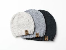 three beanies sitting next to each other on top of a white surface with brown tags