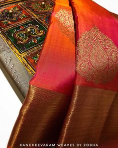 an orange and red silk saree with intricate designs on it's border, sitting on a white surface