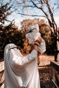 two people dressed in white are walking across a bridge and one person is covering her face with a sheet