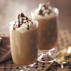 two glasses filled with hot chocolate and whipped cream on top of a table next to gold spoons