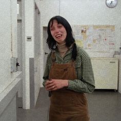 a woman in overalls standing next to a wall