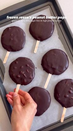 chocolate covered pops are on a baking sheet and being held up by a person's hand