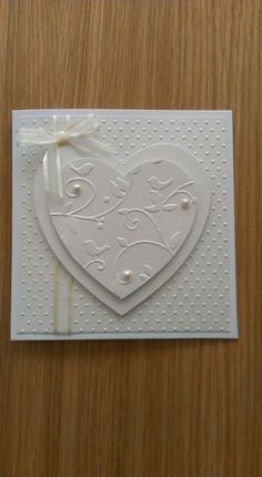 a white card with a heart and bow on the front, sitting on top of a wooden table