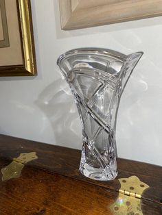 a clear glass vase sitting on top of a wooden table next to a framed painting