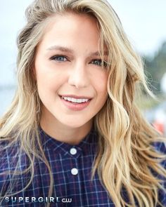 a close up of a person wearing a blue shirt and smiling at the camera with long blonde hair