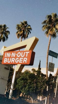 an in - n - out burger sign with palm trees and street signs behind it