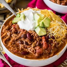 two white bowls filled with chili, beans and avocado topped with sour cream