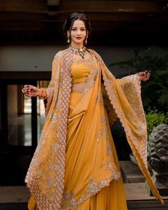 a woman in a yellow sari and gold outfit with her arms spread out to the side