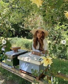 a woman wearing a hat and sitting in front of some beehives