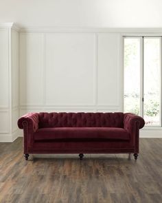 a red couch sitting on top of a hard wood floor next to a white wall