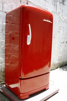 a red refrigerator sitting on top of a wooden pallet next to a brick wall