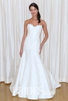 a woman standing in front of a white curtain wearing a wedding dress with an open back